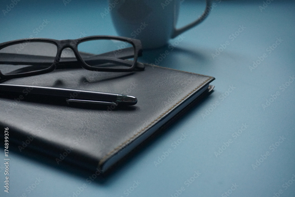 Business concept. Pen and eye glasses on black organizer on blue background,. Business concept. Pen and eye glasses on black organizer on blue background,.