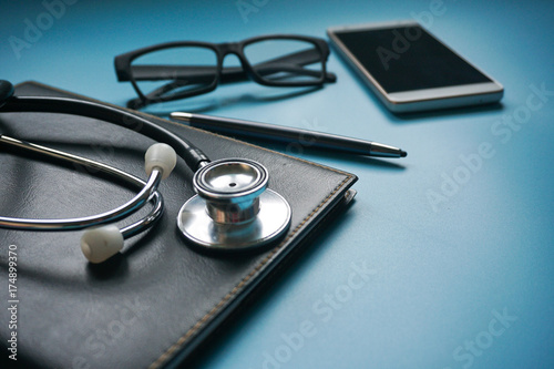 Stethoscope, black organizer, pen, eye glasses and smartphone on blue background. Healthcare concept.