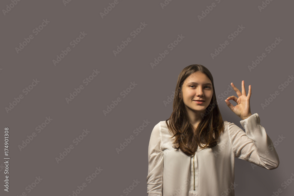 portrait of a young beautiful student girl shows sign ok. concept of success. a lot of copy space. isolated on a gray background. portrait of a young beautiful student girl shows sign ok. concept of success. a lot of copy space. isolated on a gray background.