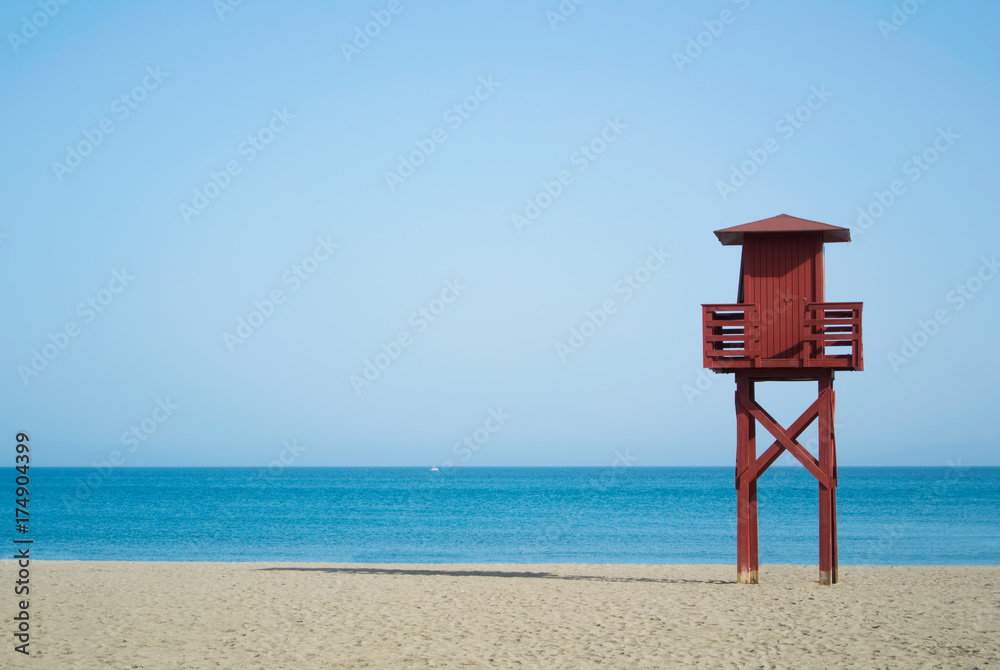 Red wooden lifeguard tower on the abandoned beach at Benalmadena, Malaga province, Spain. Beautiful view of the sea and sandy beach on sunny summer day with copy space. Red wooden lifeguard tower on the abandoned beach at Benalmadena, Malaga province, Spain. Beautiful view of the sea and sandy beach on sunny summer day with copy space.