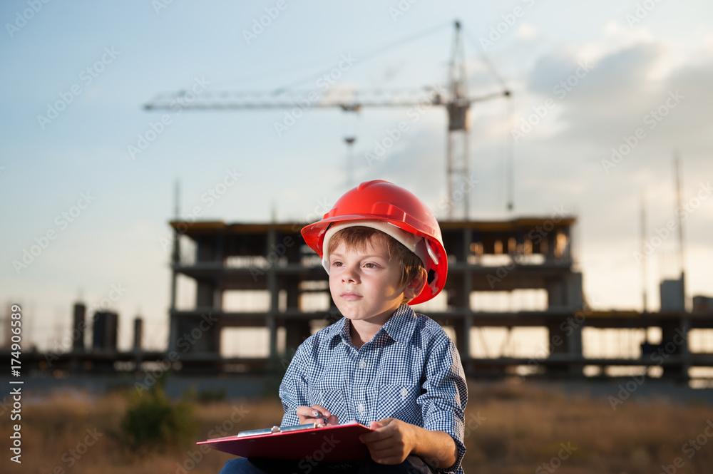 kid in orange helmet makes notes on a tablet on a construction background with a crane kid in orange helmet makes notes on a tablet on a construction background with a crane