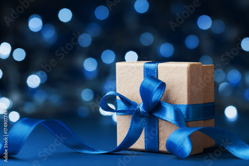 Holiday gift box or present with bow ribbon against blue bokeh background. Magic christmas greeting card.