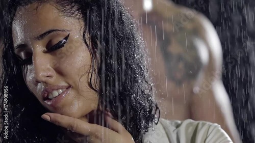 young Oriental girl with thick dark brown hair standing in the rain. in the background a naked man. she touches a gentle hand to his face