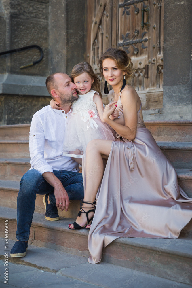 The young happy family sitting in embrace on the stairs of old building outdoors