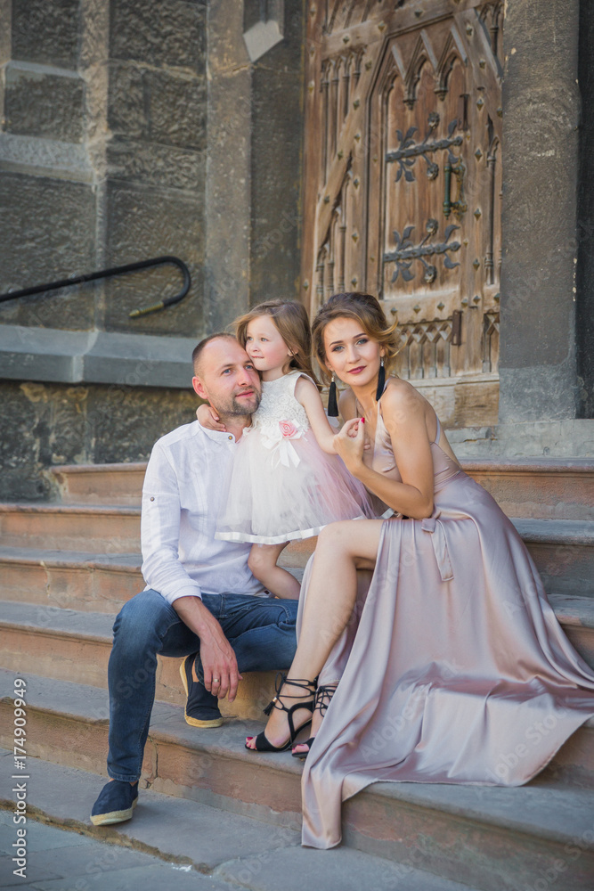 The young happy family sitting on the stairs of old building, father embracing his little cute daughter