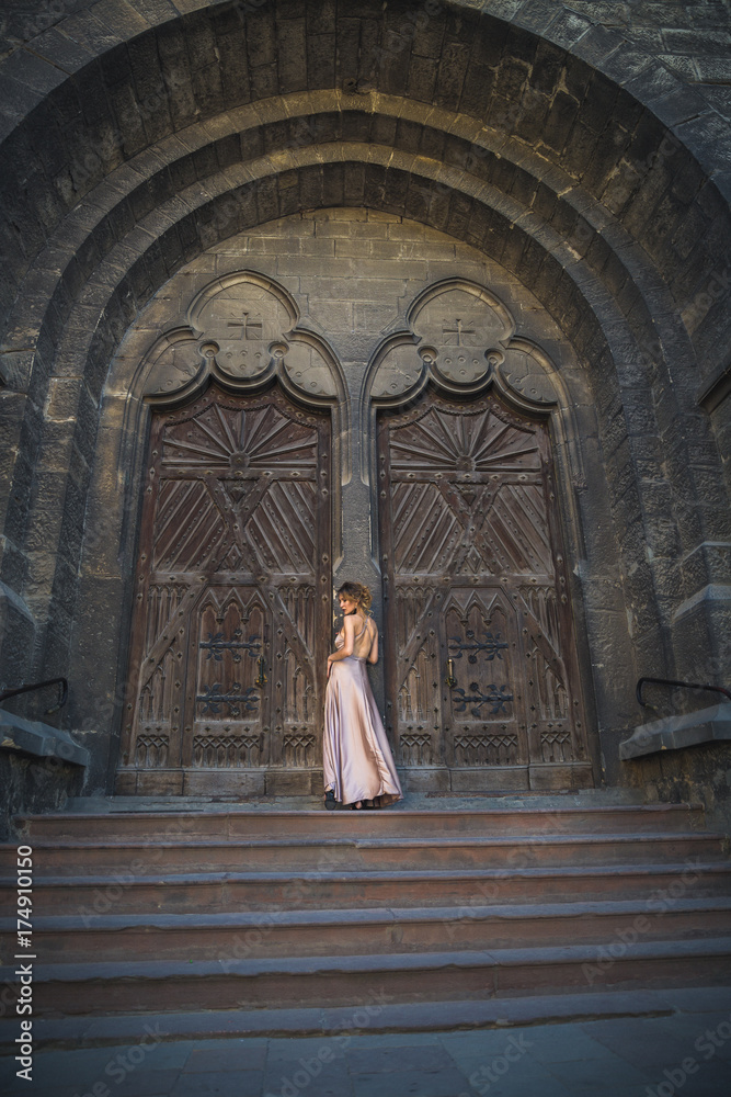 The young elegant divine woman standing outdoor on the stairs of Roman Catholic Church