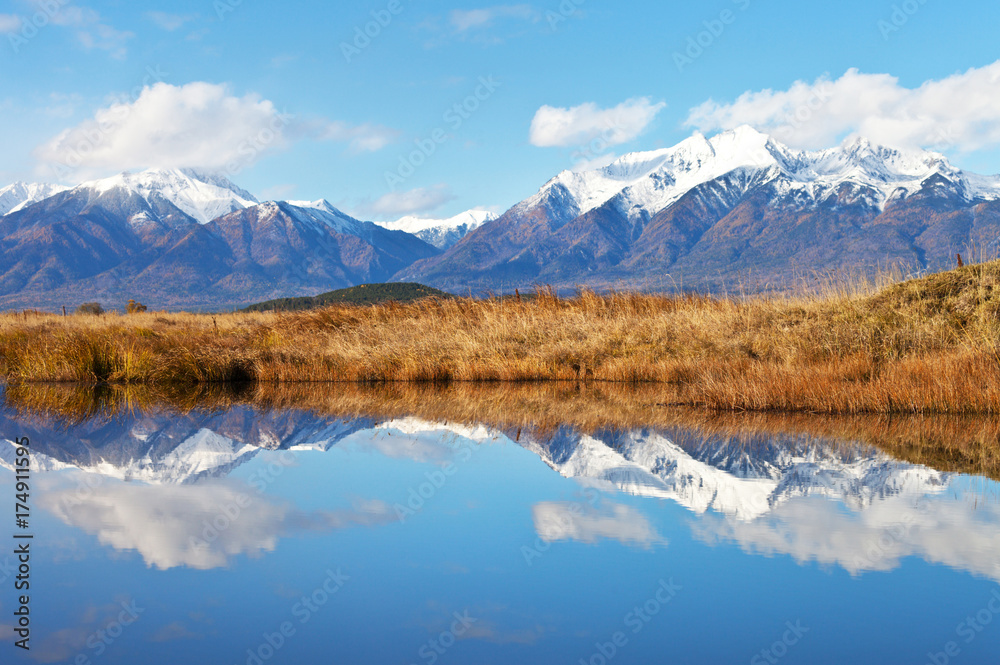 A picturesque landscape with a mirror image of a snow-covered mountain range and sky in calm blue water