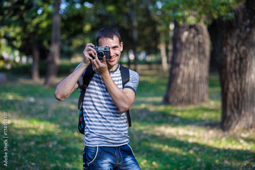 Young man taking pictures on retro camera in city park