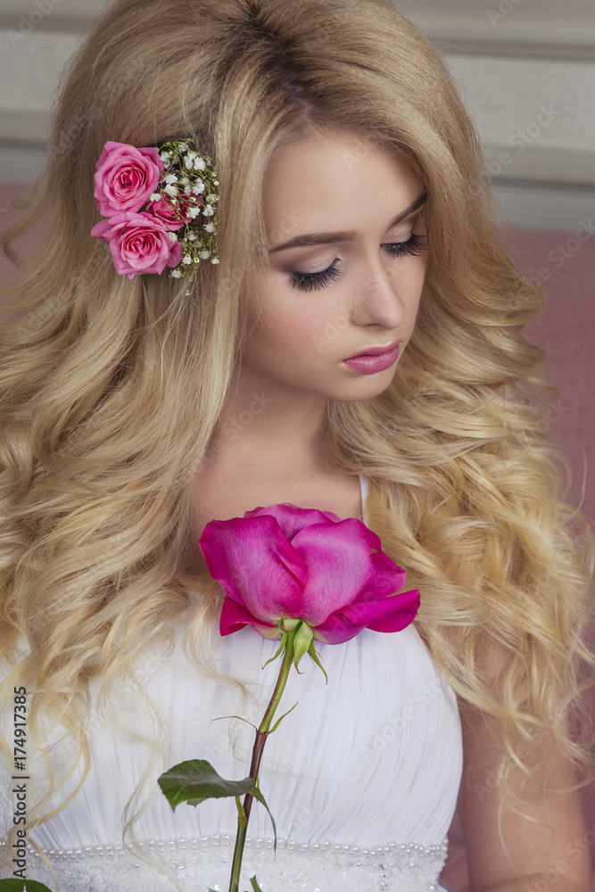 Naklejka premium Blonde with long hair in a white dress and with a rose in your hands 