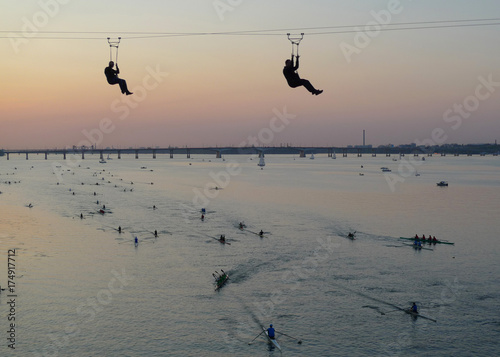 Holiday city day. Dniepr, Ukraine. Regatta 2017 held on the river Dnieper with sunset in the backgrounds. Sport action in adventure park rope. Ropeway for fun. Group of People Paddling on Kayaks. 