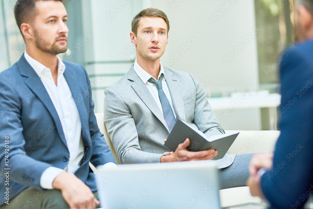 Talented team of white collar workers in suits sharing ideas concerning start-up project while having working meeting at spacious boardroom Talented team of white collar workers in suits sharing ideas concerning start-up project while having working meeting at spacious boardroom