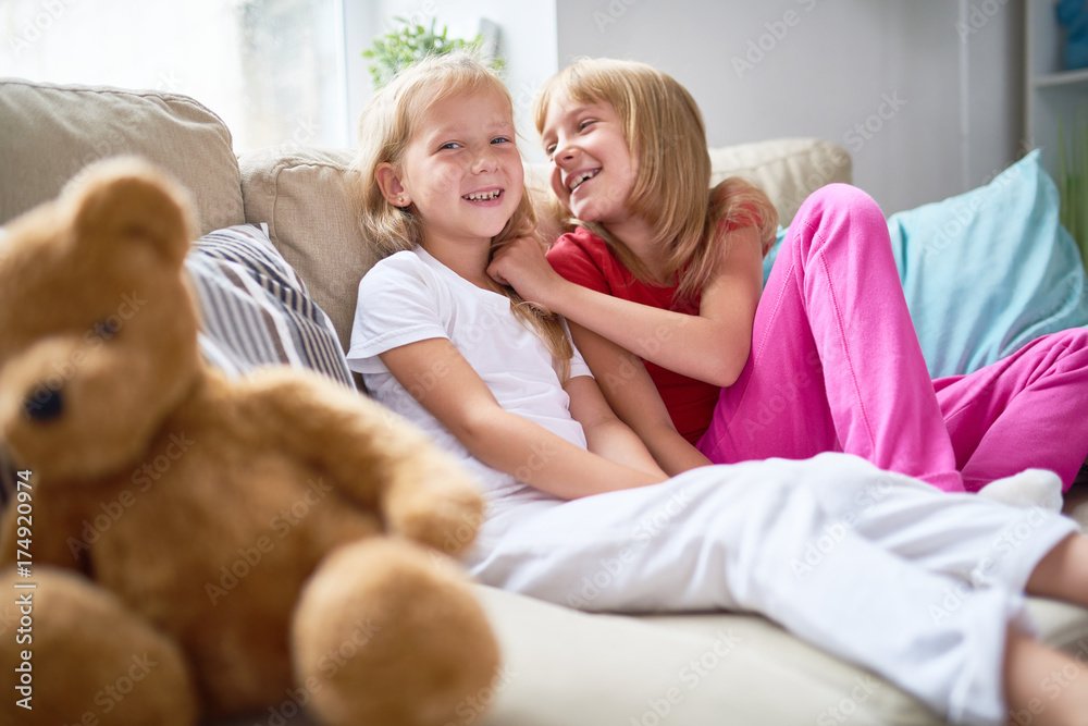 Portrait of two happy little sisters sitting on comfortable couch in cozy living room at home and smiling at camera Portrait of two happy little sisters sitting on comfortable couch in cozy living room at home and smiling at camera