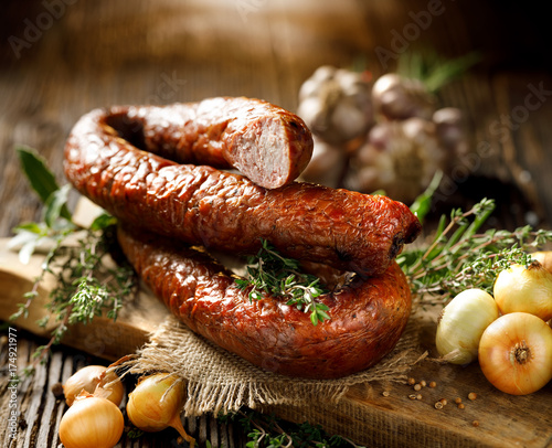 Smoked sausage on a wooden rustic table with addition of fresh aromatic herbs and spices, natural product from organic farm, produced by traditional methods