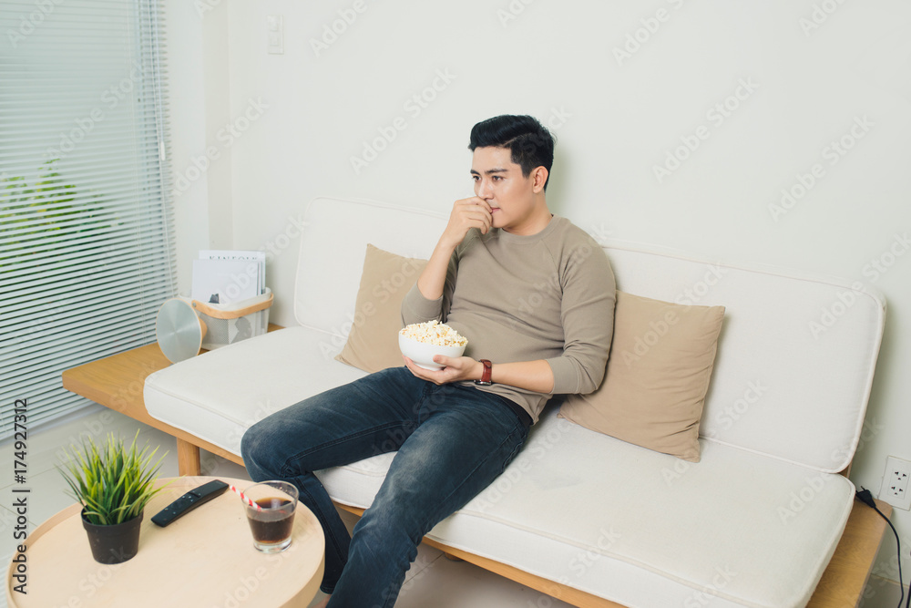 Bored asian man watching tv on the couch at home in living room