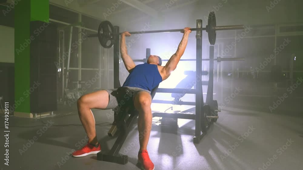 The man doing bench press in the gym on the bright light background The man doing bench press in the gym on the bright light background