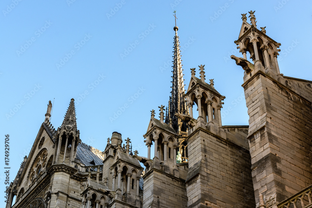 Close-up view from below of the spire of Notre-Dame de Paris cathedral with buttresses, pinnacles and gargoyles in the foreground.