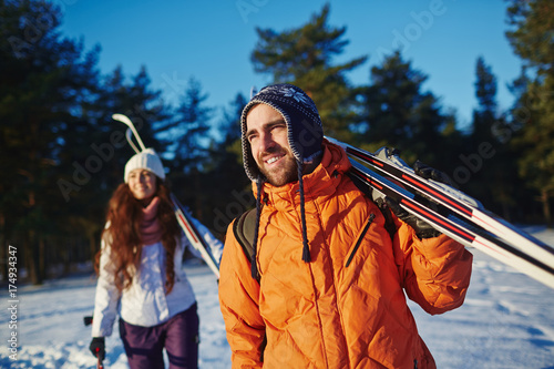 Young sporty couple with skiing equipment looking ahead while choosing place for skiing