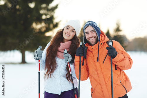 Joyful amorous couple of skiers in winterwear looking at camera