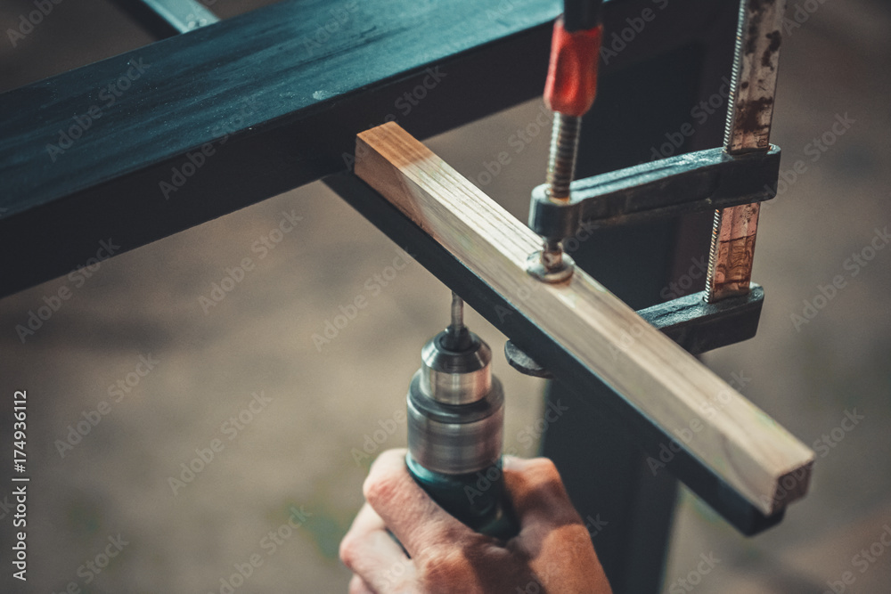 Obraz premium Man using the drill makes a hole in wood and iron strap. The process of making desk, furniture