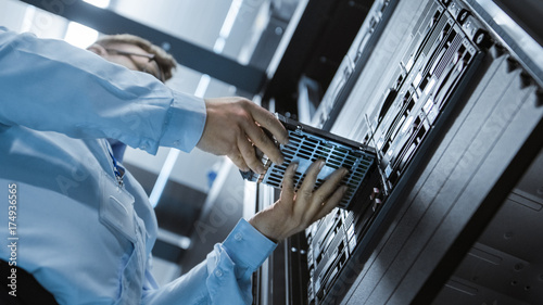 Canvas Print Low Angle Shot In Fully Working Data Center IT Engineer Installs Hard Drive into Server Rack