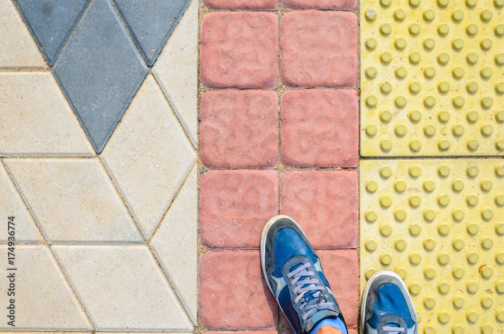 View from the First Person to his Feet, Standing in Front of the Sidewalk with Tactile Tiles to Navigate Blind People. Blue Sneakers on Yellow Tactile Paving Slabs.