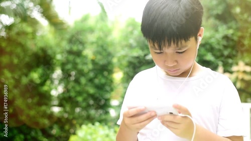 Slow motion of preteen Asian Thai boy is using smartphone to play game in his home garden. Technology and health concept photo