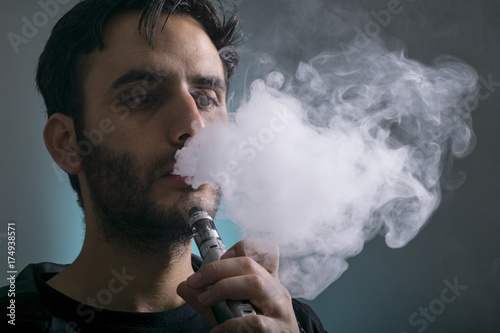 young man vape electronic cigarette cloud by using a mod, smoke tricks of vaping device background. 