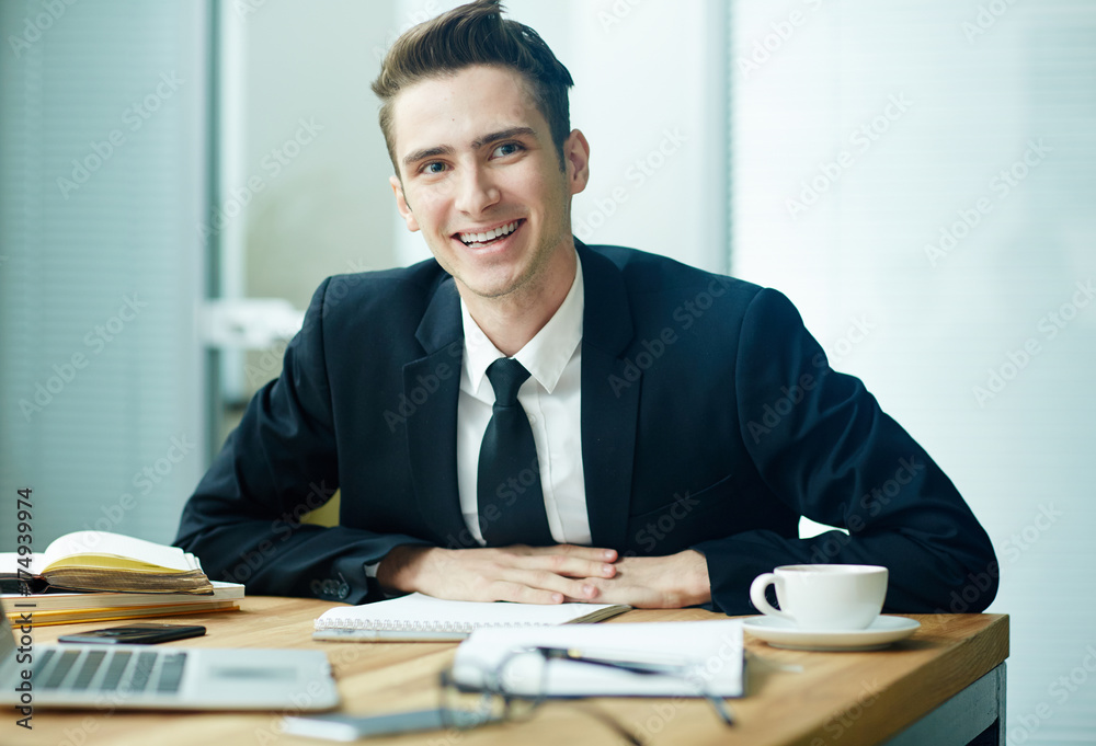 Young smiling elegant man looking at camera at his workplace Young smiling elegant man looking at camera at his workplace