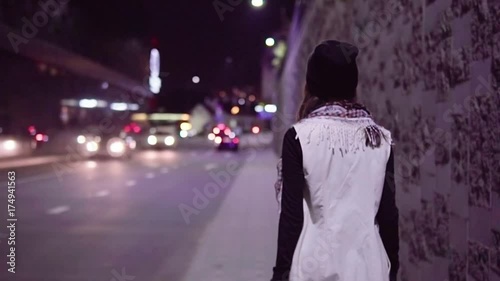 Young woman walking along night city street, slow motion
