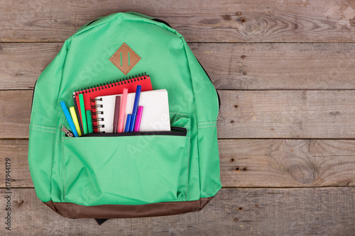 Backpack and school supplies: notepad, felt-tip pens on brown wooden table
