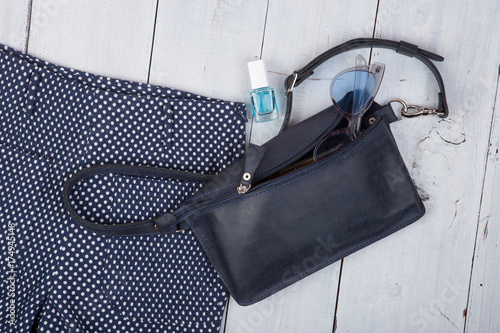 Female fashion stuff - bag, trousers, sunglasses, nail polish on white wooden background