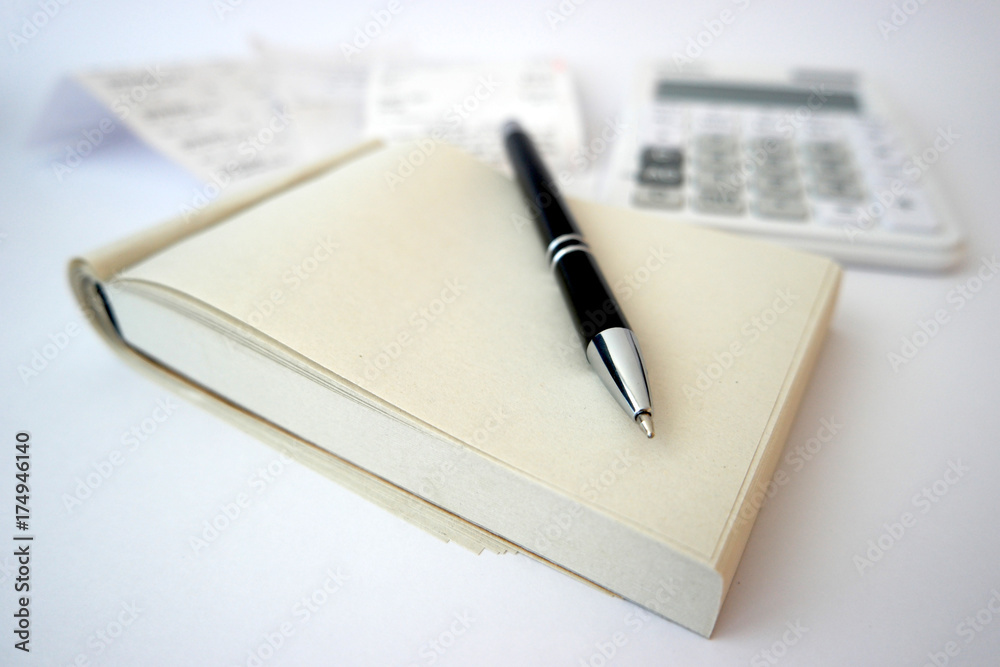 A black pen on top of a note pad with receipts and calculator in the background. Taking notes of expenses and budgeting A black pen on top of a note pad with receipts and calculator in the background. Taking notes of expenses and budgeting
