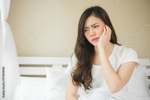 Asian woman have a toothache on white bed in white bedroom in morning