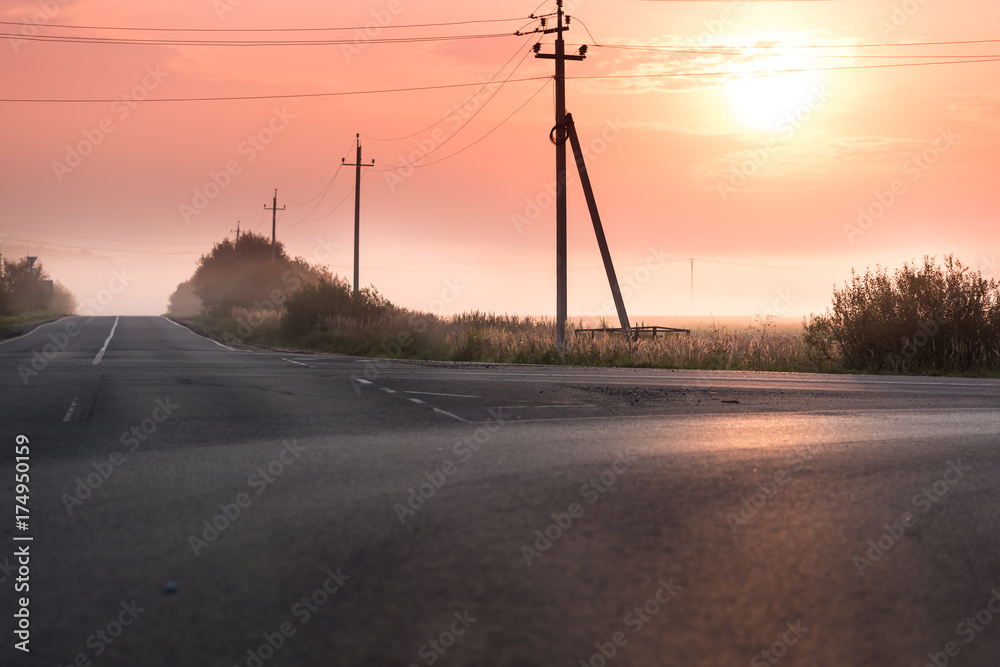 The road in the fog. Red sunrise. Electric poles near the road in the morning The road in the fog. Red sunrise. Electric poles near the road in the morning