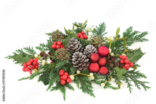 Christmas decorative display red bauble decorations, holly, ivy, mistletoe, cedar and juniper leaf sprigs and pine cones on white background.