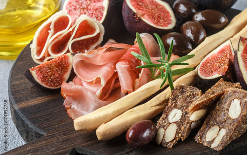 Appetizer of jamon, salami, bread sticks, Kalamata olives and figs on a cutting Board. Italian antipasti. Selective focus