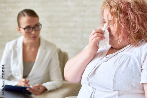Portrait overweight woman crying wiping tears with tissue during therapy session with female psychiatrist