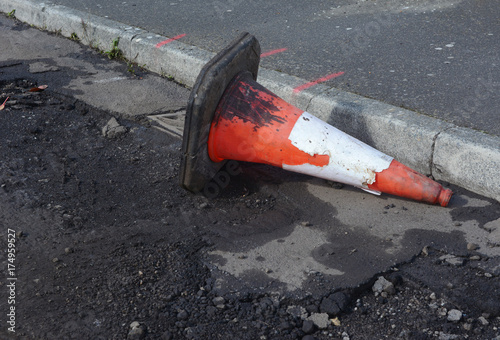 Damaged traffic cone in gutter, road undergoing repairs photo