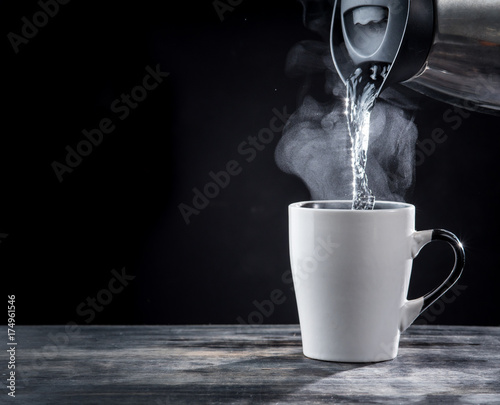Fototapet Pouring hot water into into a cup on a black background