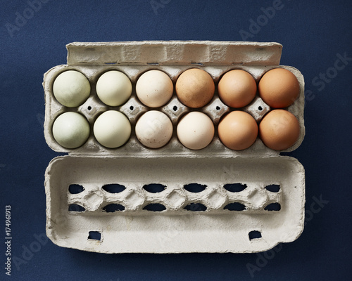 Chicken eggs of various natural colors in a carton on a navy background