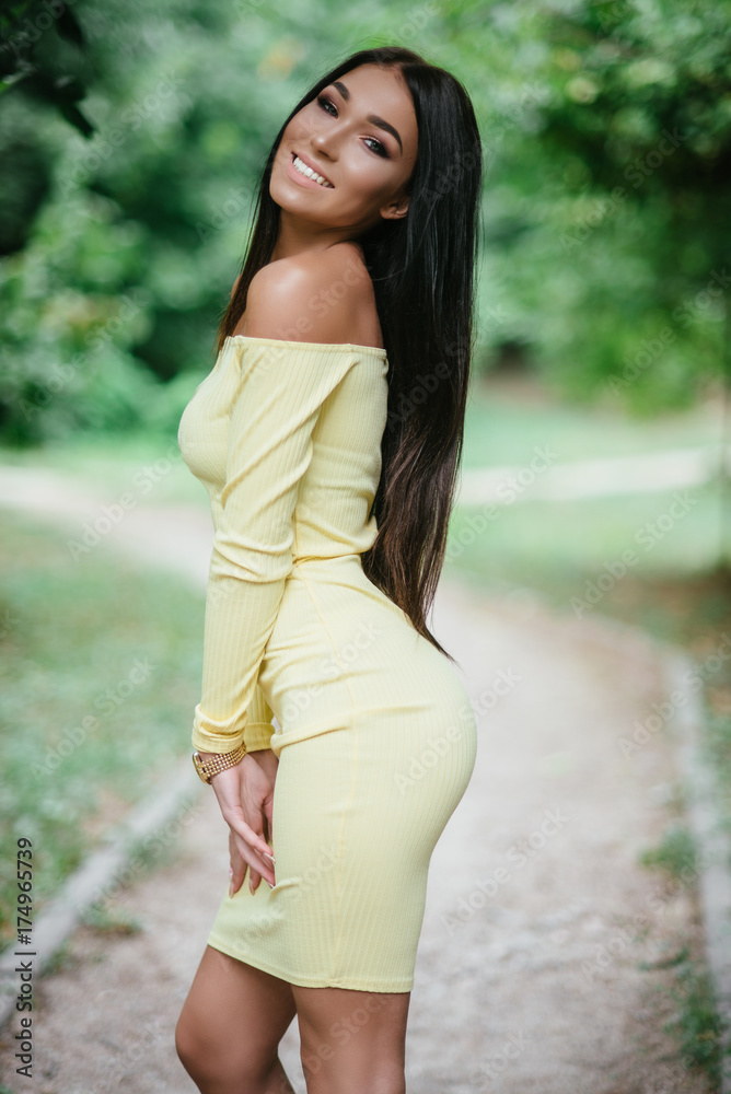 young beautiful brunette woman posing in yellow elegance dress at green summer park 