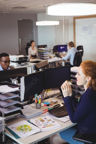 Businesswoman eating snack while colleagues working in creative