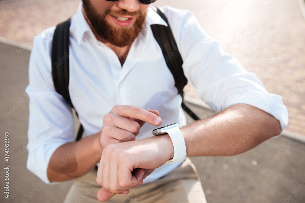 Cropped close up image of smiling bearded man using wristwatch