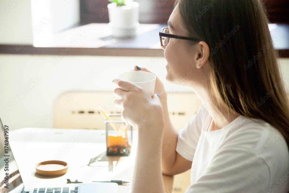 Female employee taking a break from work on laptop computer, enjoying a cup of tea or coffee at workplace desk in small home office. Close up view. Relaxation, positive thoughts in workplace concept Female employee taking a break from work on laptop computer, enjoying a cup of tea or coffee at workplace desk in small home office. Close up view. Relaxation, positive thoughts in workplace concept