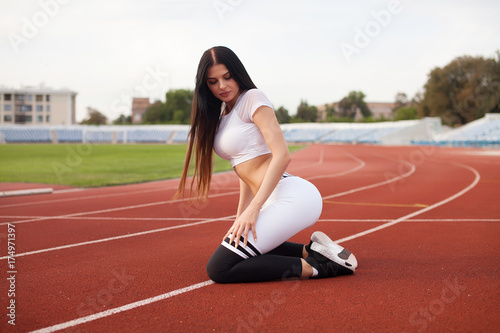 Beautiful smiling young woman, stretching on a running track