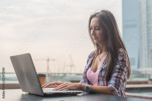 Young woman using a laptop working outdoors. Female looking at the screen and typing on keyboard