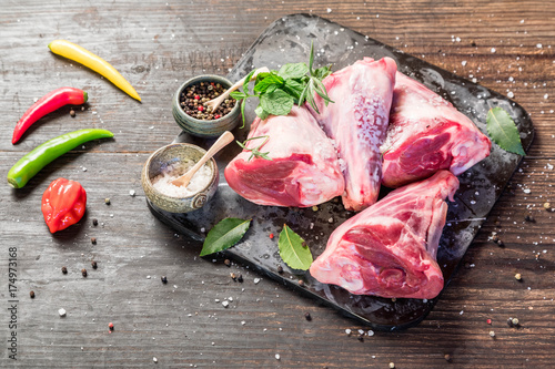 Raw lamb shanks with salt and pepper on stone tray on rustic wooden table, selective focus