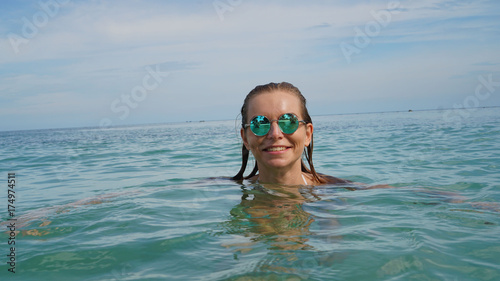 Happy woman in sunglasses relaxing and smiling in the sea water over blue sky background. Holiday vacation concept