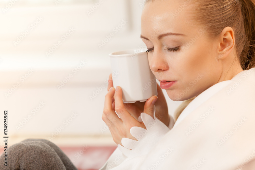 Woman lying on sofa under blanket drinking tea Woman lying on sofa under blanket drinking tea