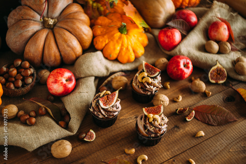 Autumn tasty cupcakes with ginger and chocolate on a wooden background of autumn harvest. Pumpkins  patsons  apples  nuts.